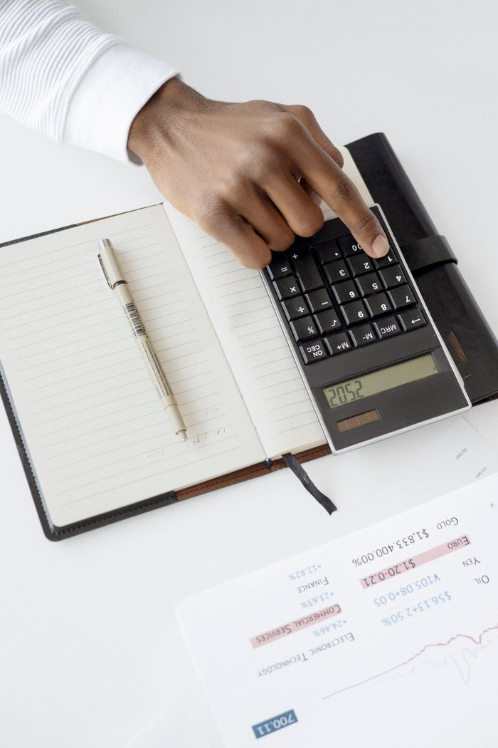 gallery-03 A hand using a calculator with financial documents and notebook, depicting an office setup for financial analysis.