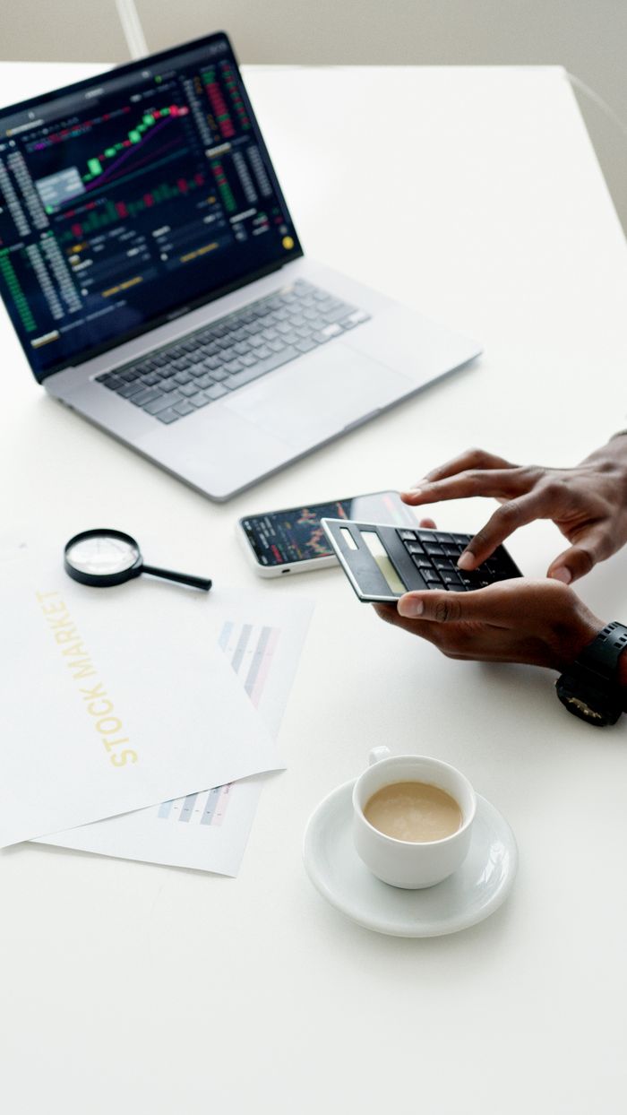 gallery-04 A businessman using a laptop and smartphone to analyze stock market trends indoors.